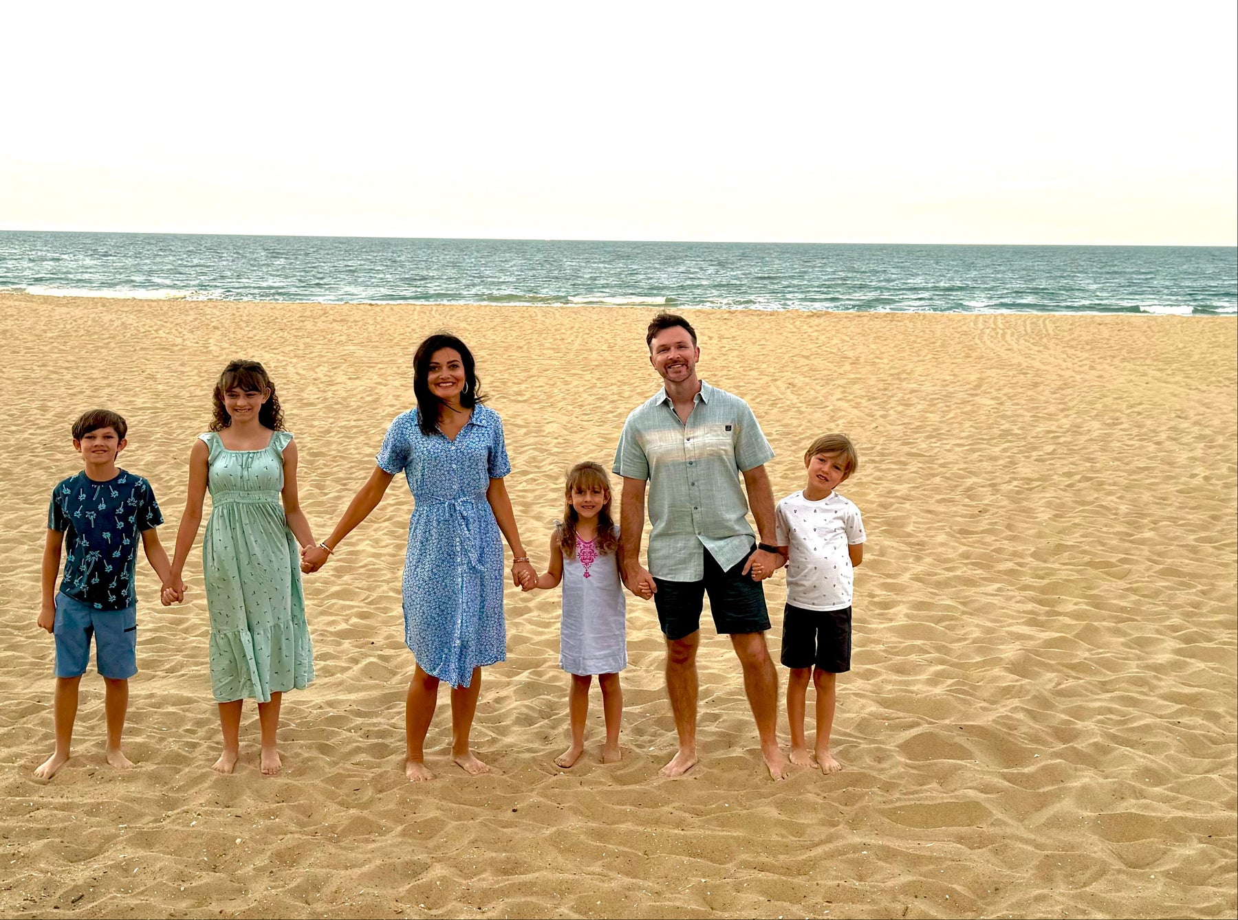 Family of six standing on a sandy beach with ocean in the background